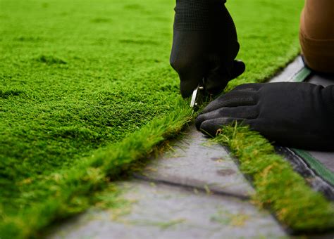 Egy ember sniccerrel méretre vágja a műfüvet erkélyen